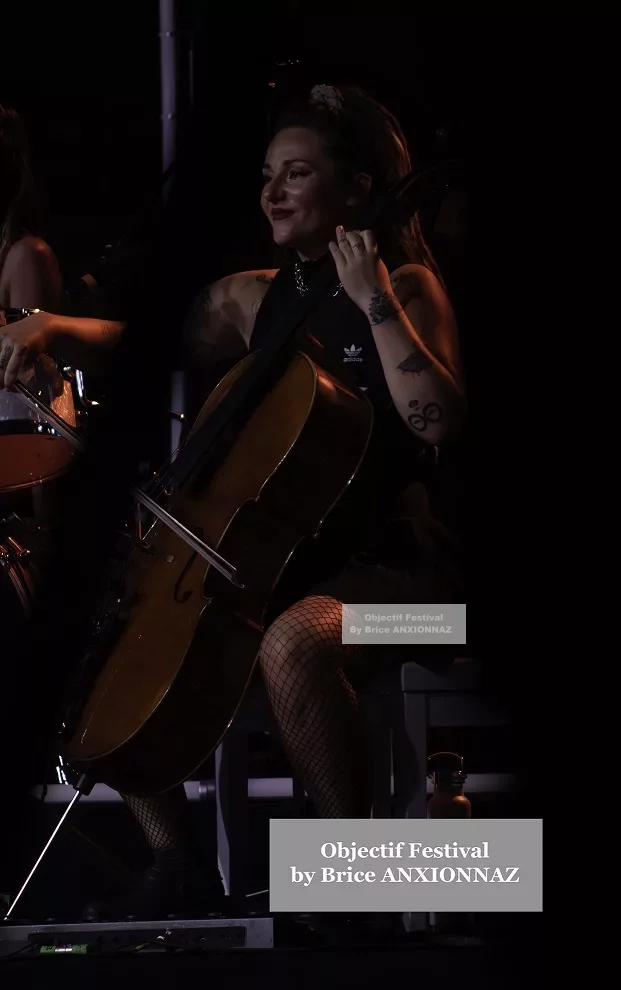 Une musicienne joue du violoncelle sur scène, éclairée par des lumières tamisées, portant une tenue noire avec des collants en résille, créant une ambiance artistique et intime. Lej, Hyeres (06/08/2024)