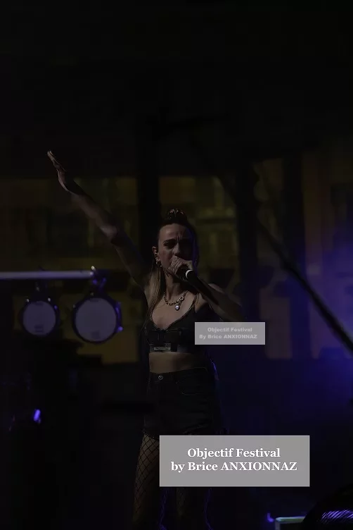 Une artiste se produit sur scène, vêtue d'un haut noir et de collants, avec des lumières tamisées créant une ambiance dynamique et énergique. Lej, Hyeres (06/08/2024)