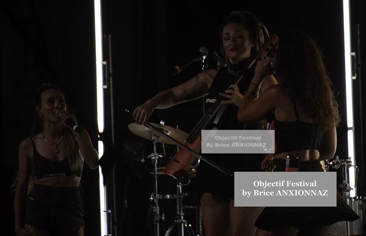 Deux musiciennes se produisent sur scène, l'une chantant et l'autre jouant du violoncelle, avec des éclairages dramatiques et une ambiance dynamique, vêtues de tenues noires. Lej, Hyeres (06/08/2024)