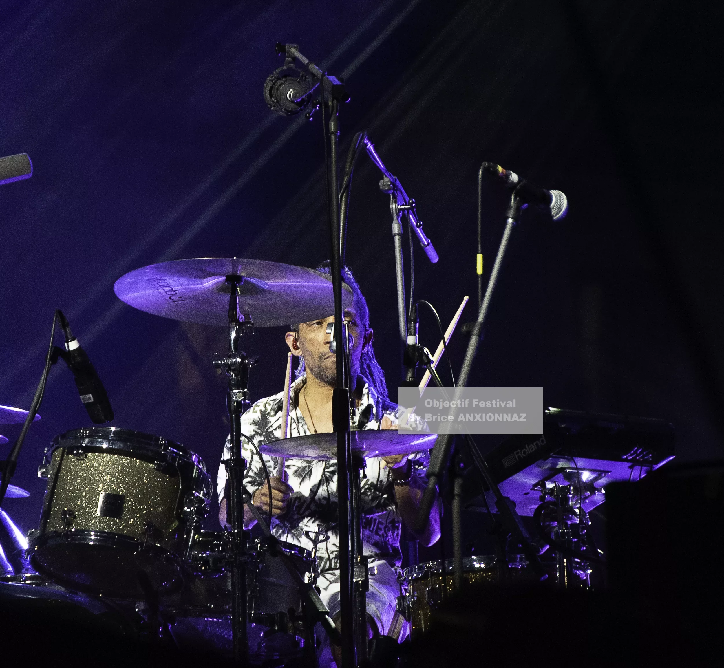 Louis Bertignac — Un batteur joue sur scène, entouré de cymbales et de micros, sous des lumières violettes, créant une ambiance dynamique et énergique. 21 07 2026, Hyeres (21/07/2026)
