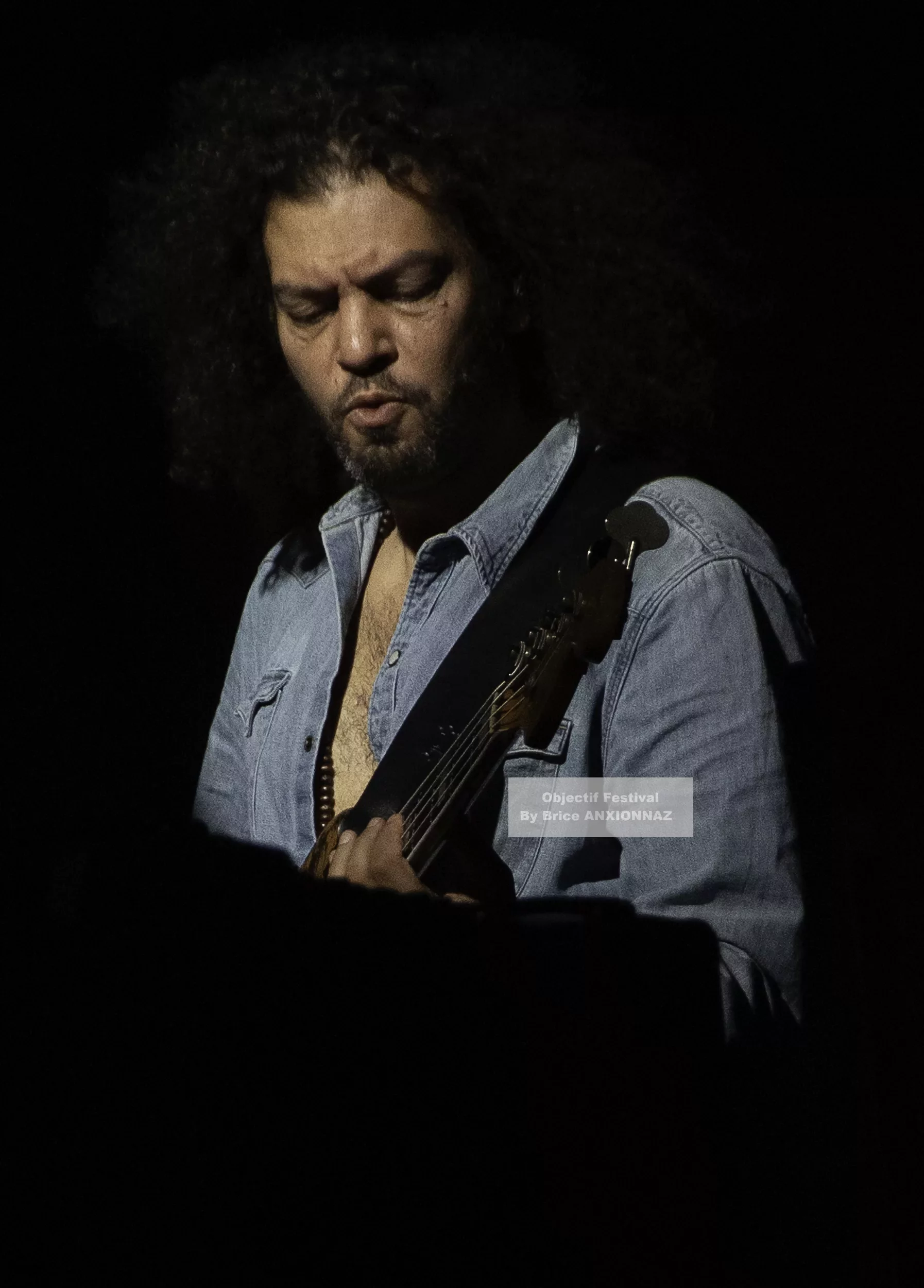 Louis Bertignac — Un musicien joue de la guitare dans une ambiance sombre, éclairé par une lumière douce, portant une chemise en denim, avec des cheveux bouclés et une expression concentrée. 21 07 2026, Hyeres (21/07/2026)