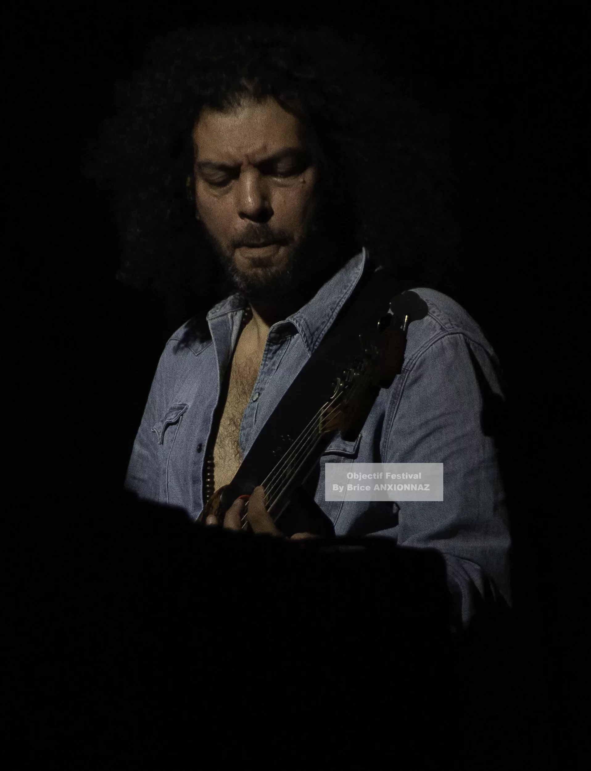 Louis Bertignac — Un musicien joue de la guitare dans une ambiance sombre, éclairé par une lumière tamisée, portant une chemise en denim, avec des cheveux bouclés et une expression concentrée. 21 07 2026, Hyeres (21/07/2026)