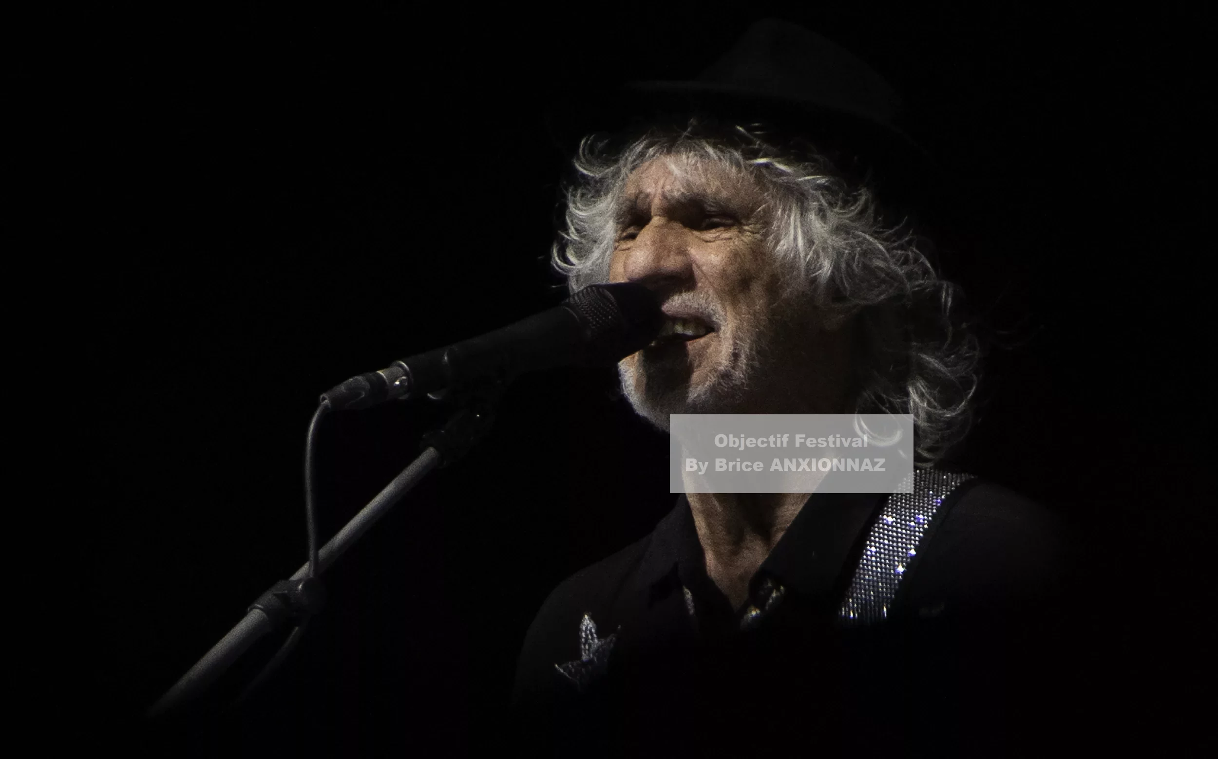 Louis Bertignac — Un homme chante au microphone, vêtu d'une chemise noire ornée d'un détail brillant, avec des cheveux gris et bouclés, sur fond sombre, créant une ambiance intimiste. 21 07 2026, Hyeres (21/07/2026)